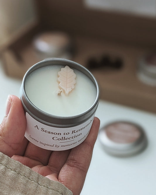 Hand holding a small candle in a tin with a visible label, set against a blurred background.