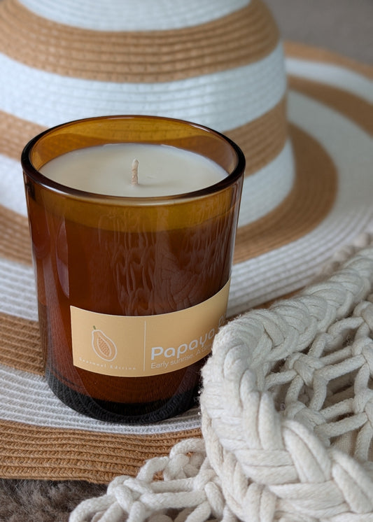 Candle in a brown glass jar with a label on a woven surface