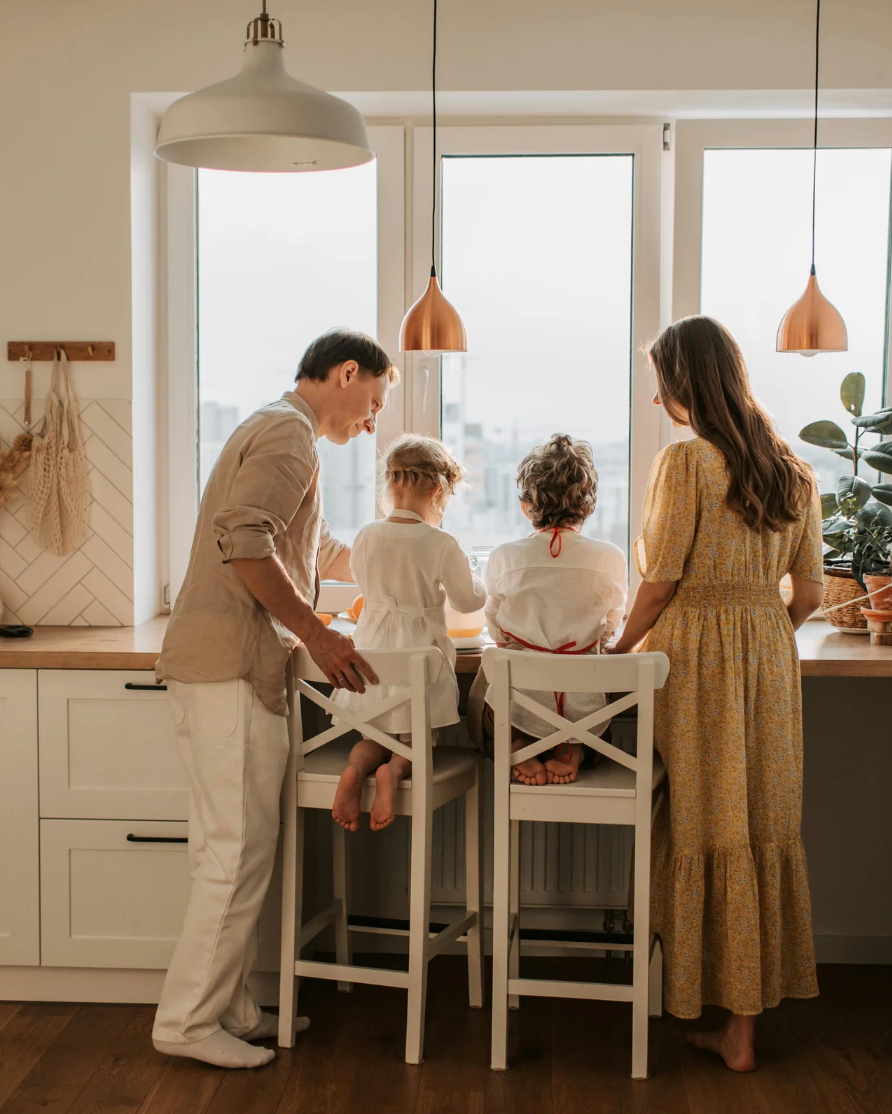 Family of four in a modern kitchen with large windows.