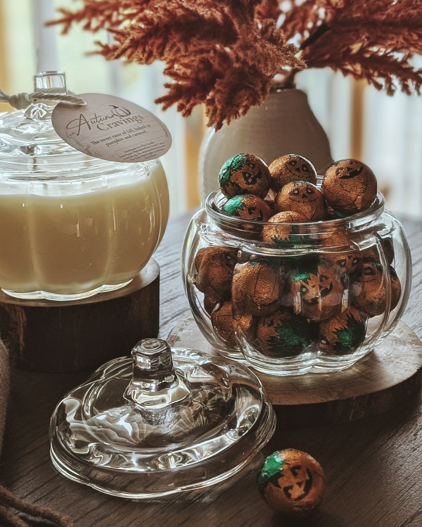Decorative setup with a candle, jar of candies, and dried plants on a wooden surface.