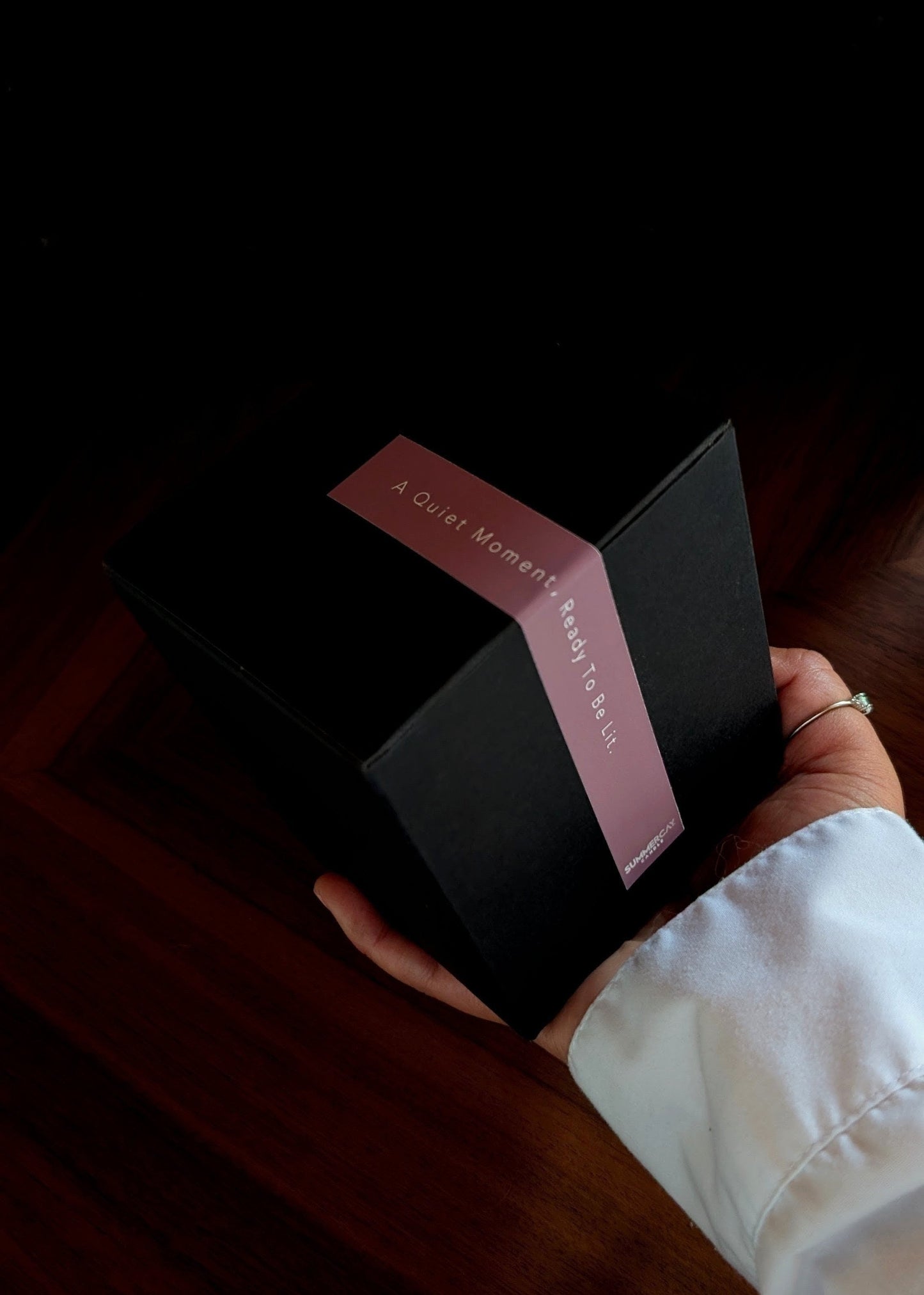 Hand holding out a black gift box with a label and a dark background.