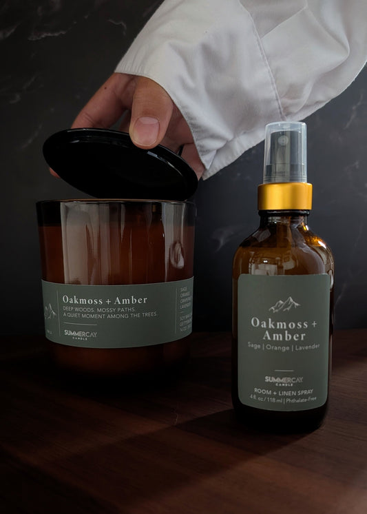 Candle and bottle labeled 'Oakmoss & Amber' on a dark surface