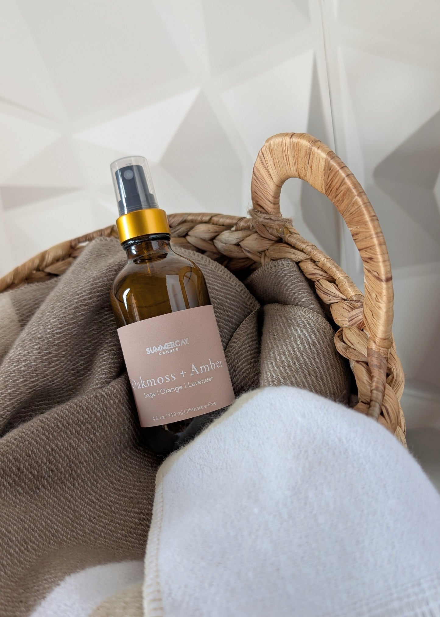 Oakmoss + amber room and linen spray in a woven basket with a neutral color blanket