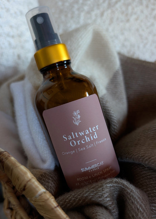Bottle of Saltwater Orchid room spray with a pink label on a textured surface