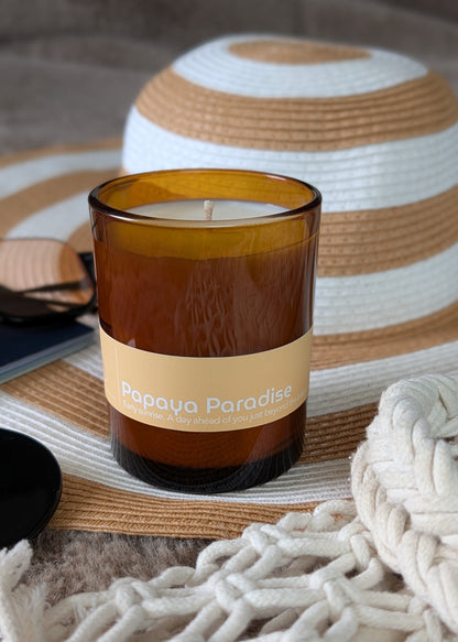 Papaya Paradise amber glass candle sitting on a beach hat next to a woven beach bag