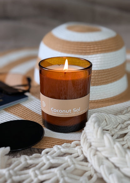 Coconut Sol scented amber glass candle with a summer beach hat and bag. 