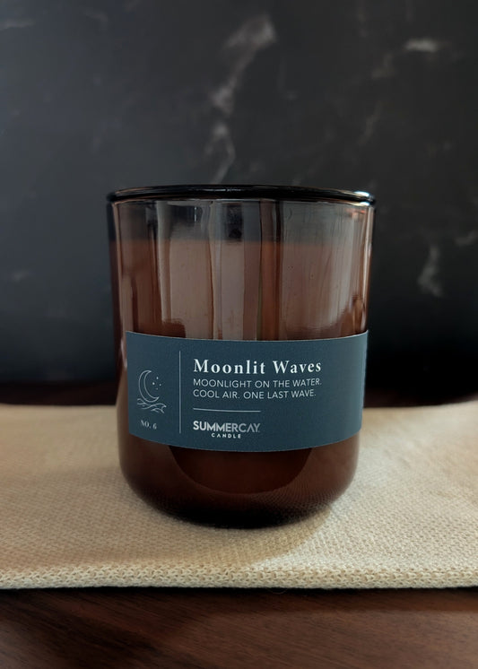 Candle labeled 'Moonlit Waves' on a textured surface with a dark background
