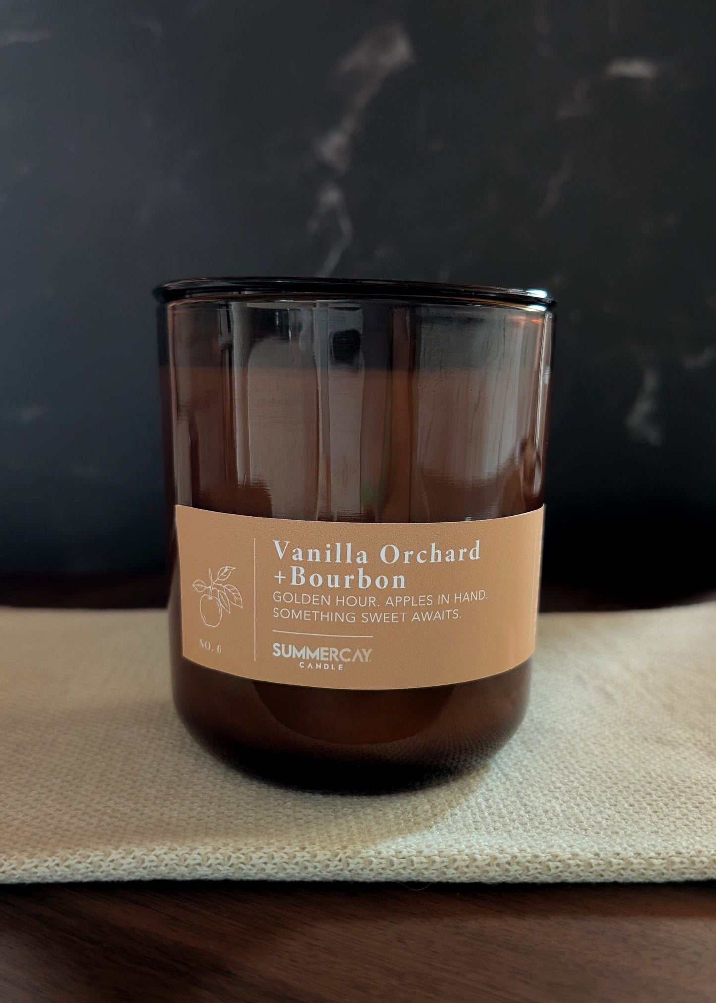 Vanilla Orchard Bourbon candle on a dark surface with a blurred background
