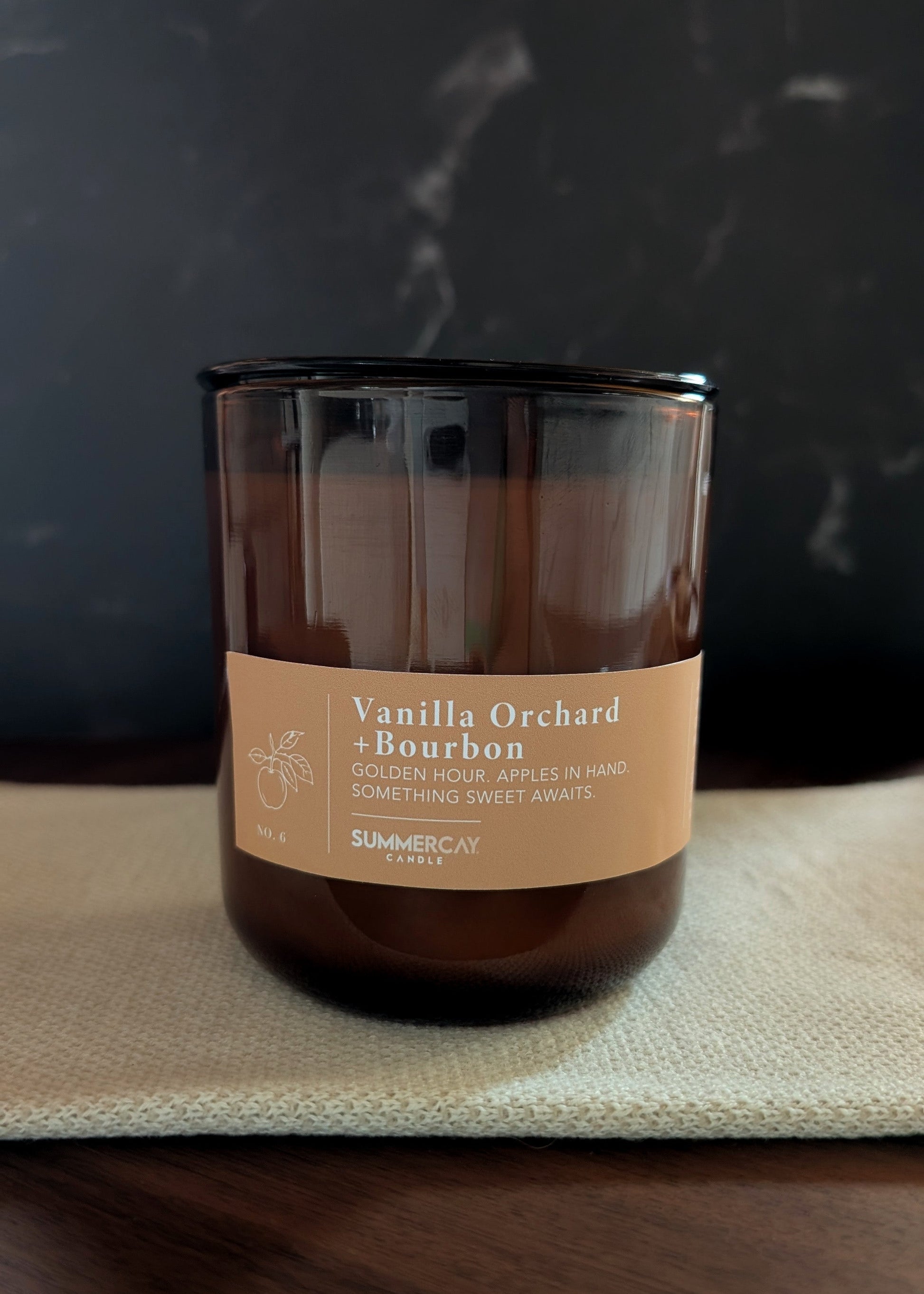 Vanilla Orchard Bourbon candle on a dark surface with a blurred background