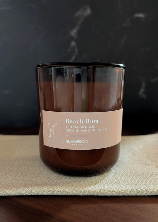 Beach Bum scented candle in an amber glass vessel with black lid and dark background. 