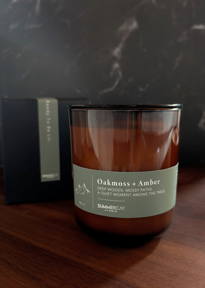 Candle labeled 'Oakmoss & Amber' on a wooden surface with a dark background