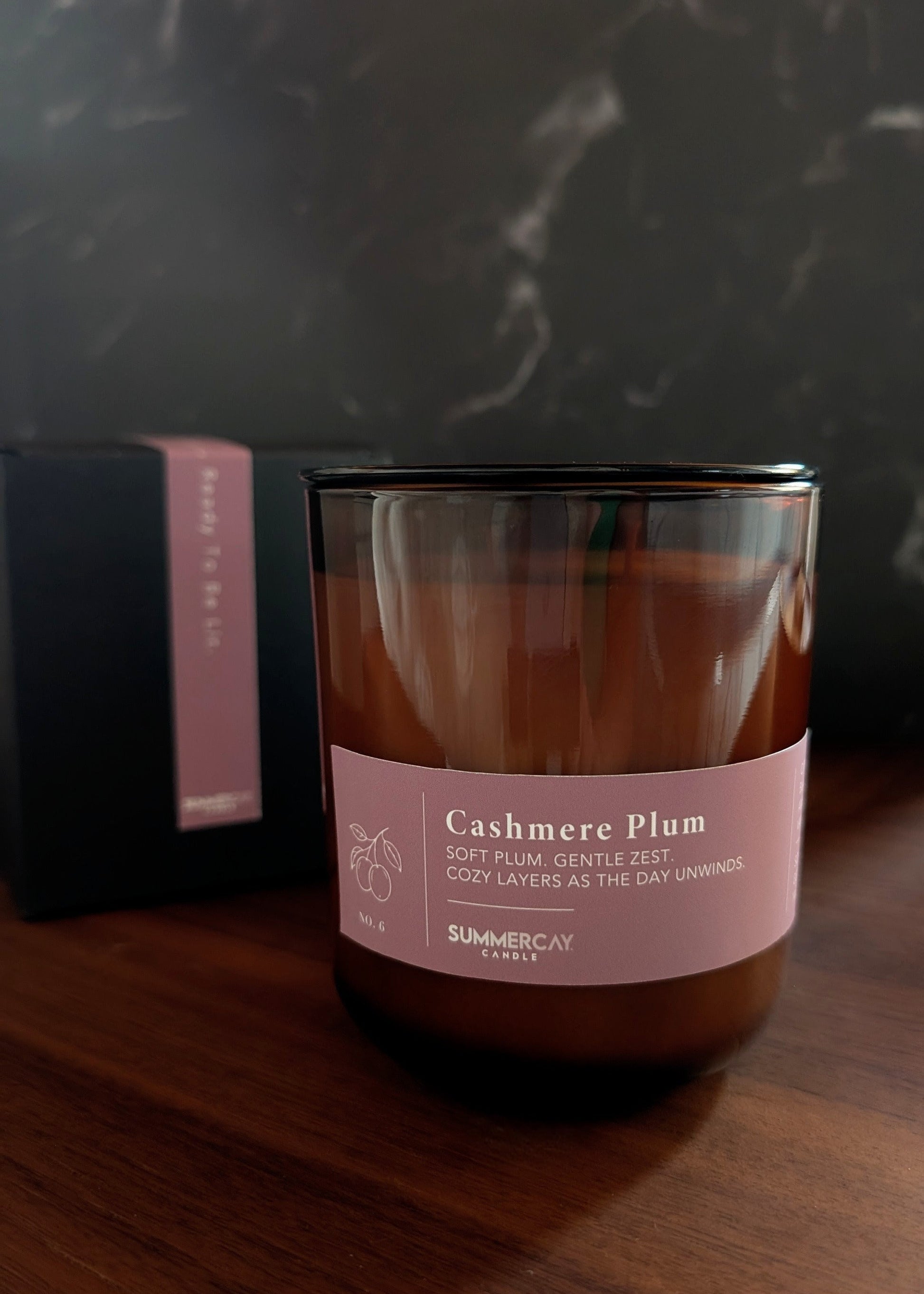 Cashmere Plum candle with gift box behind it with a dark background.