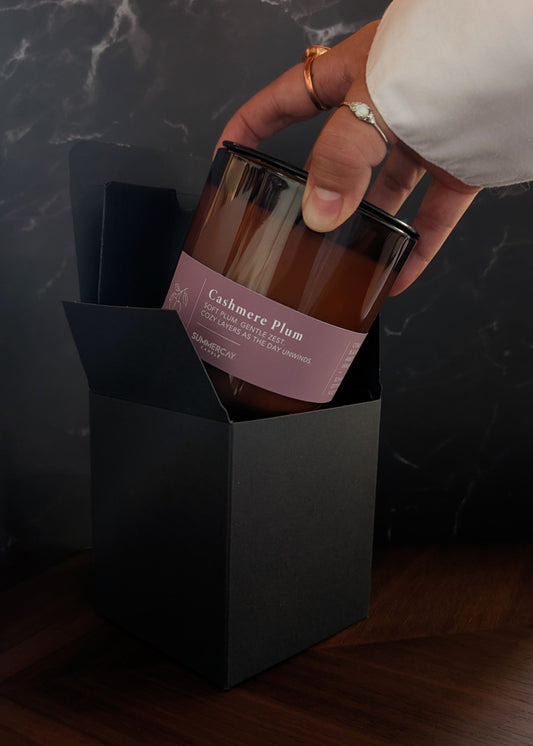 hand pulling out a Cashmere Plum candle from gift box with a dark background.