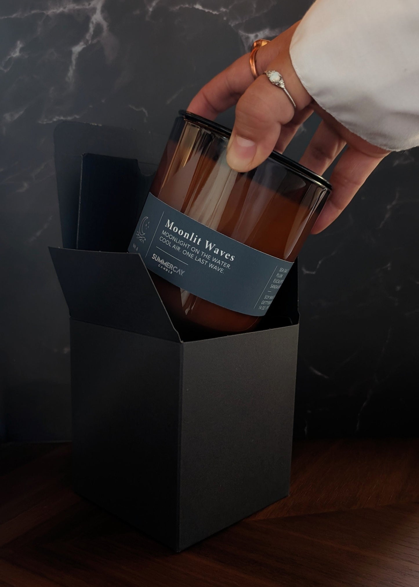 hand pulling out an amber glass candle from gift box and dark background