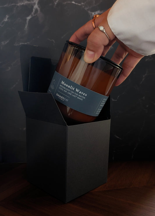 hand pulling out an amber glass candle from gift box and dark background