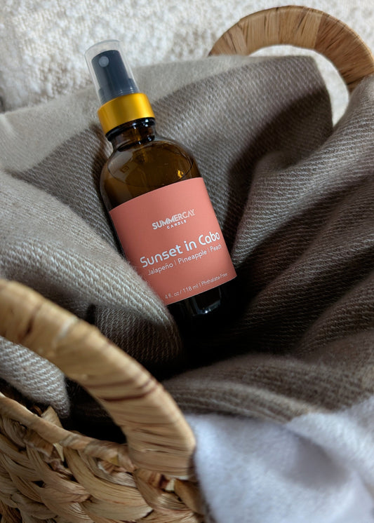 Sunset Cabo room spray in a woven basket with soft blanket.