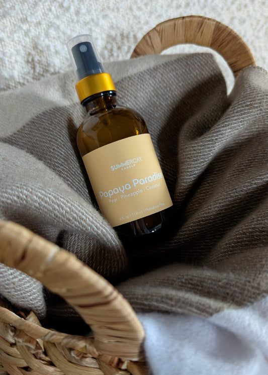 Papaya Paradise room spray in a woven basket with a soft blanket.