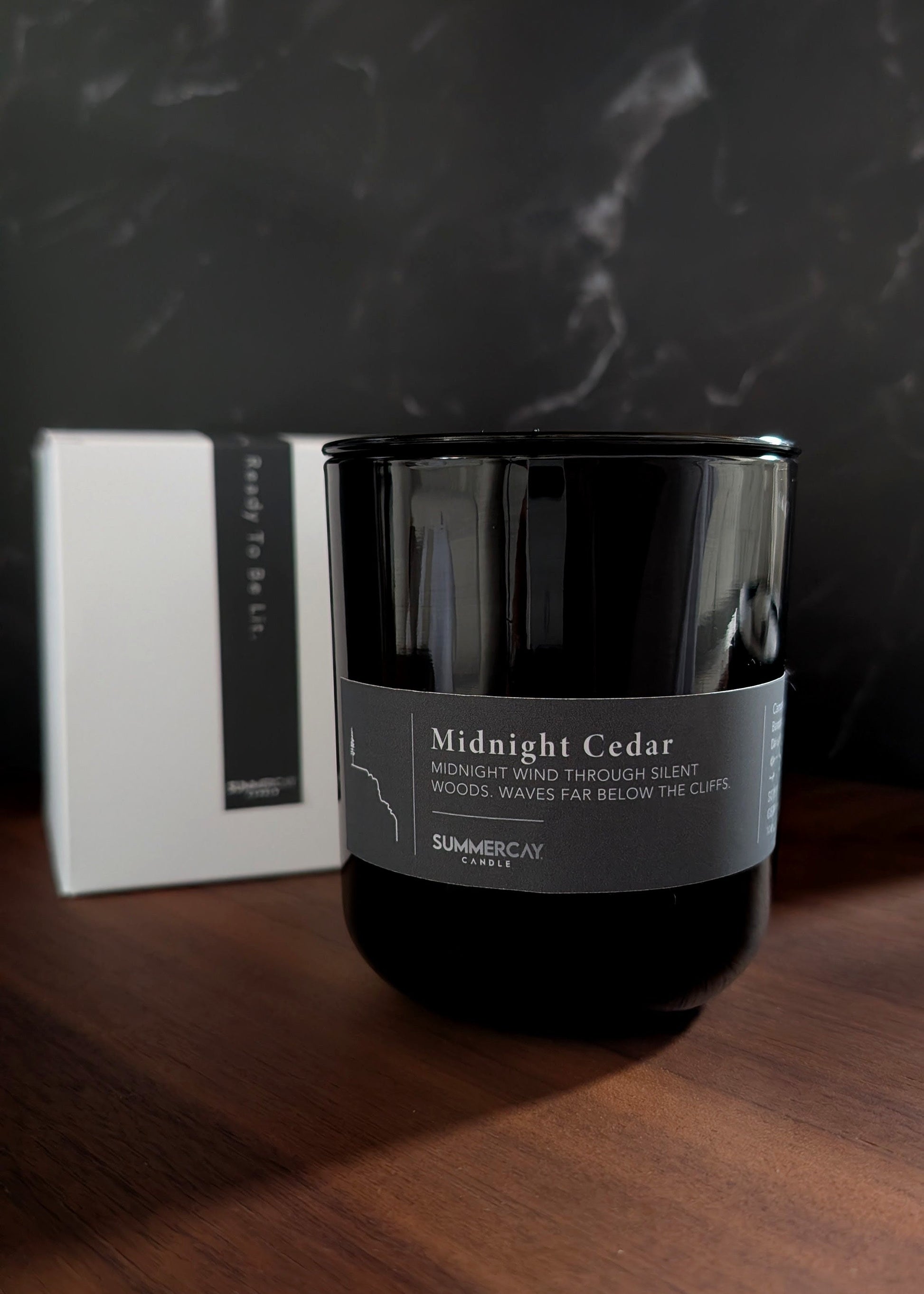 Black candle labeled 'Midnight Cedar' on a wooden surface with a dark marble background