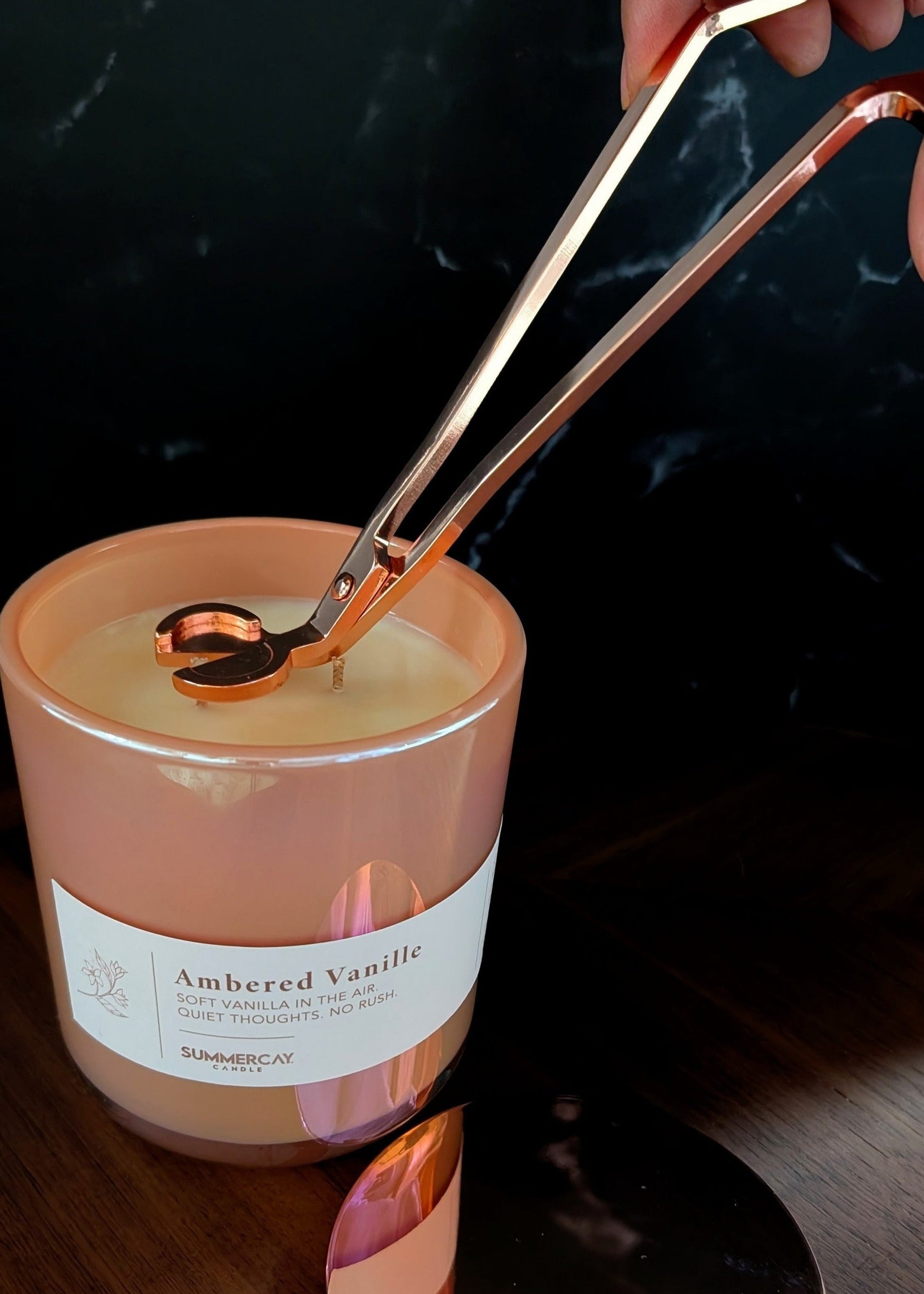 Hand holding rose gold wick trimmers up to a candle wick