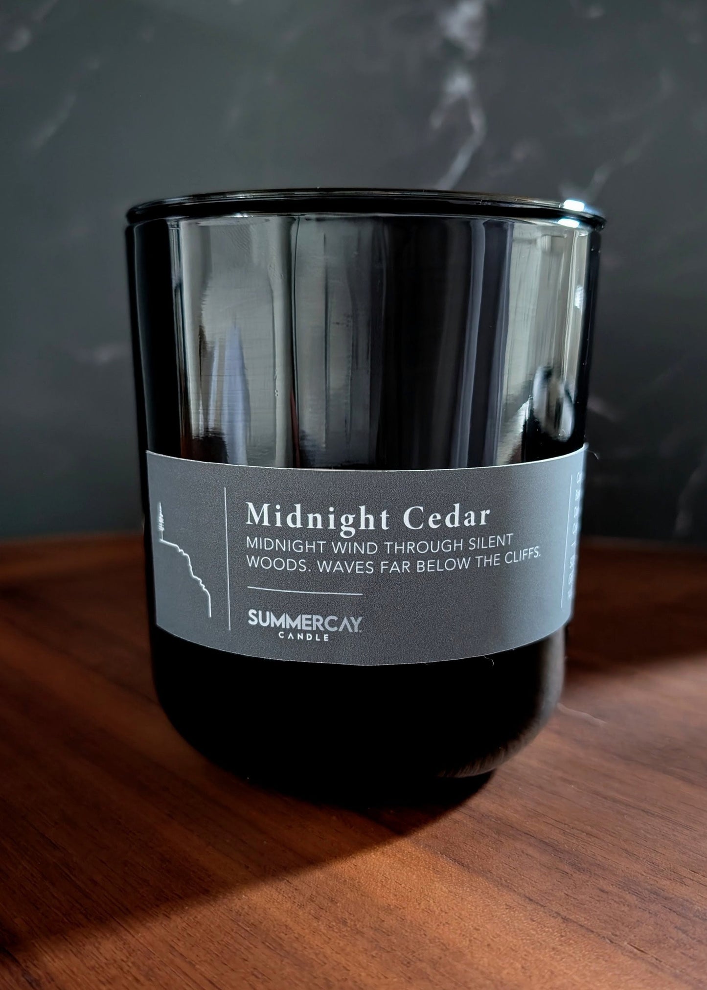 Midnight Cedar black vessel candle on a wooden table dark setting.