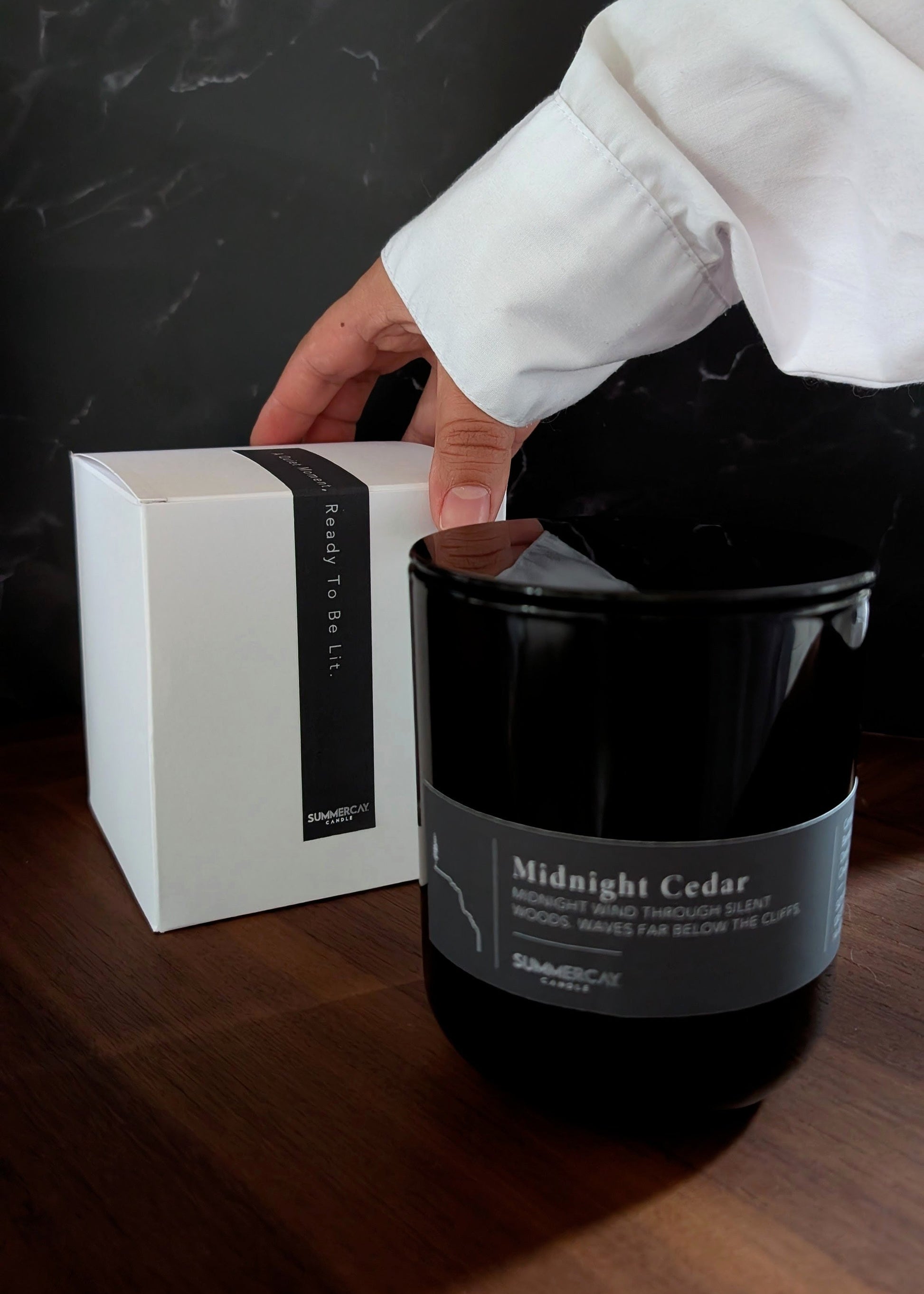 Black candle labeled 'Midnight Cedar' with a white box on a dark surface