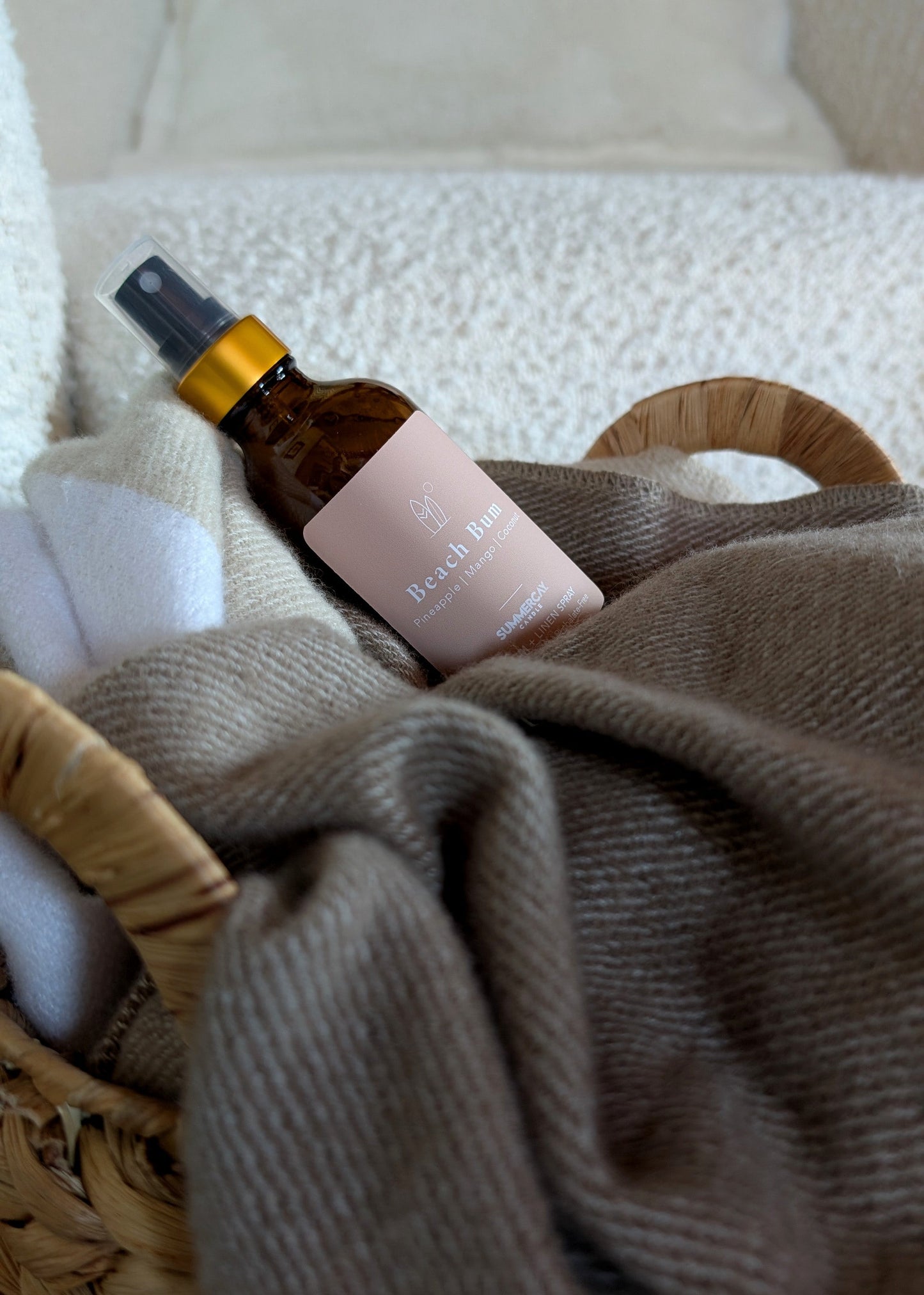 beach bum room spray in a woven basket with blanket and a white background.