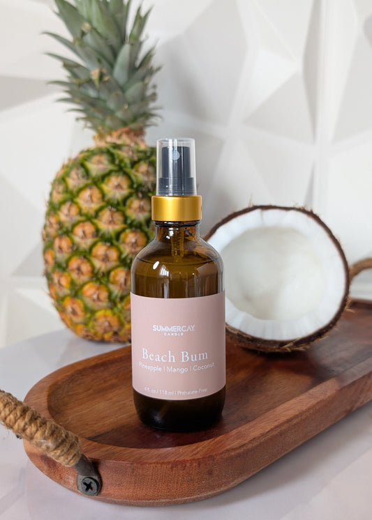 Beach Bum room spray sitting on a wooden tray with a pineapple and opened coconut in the background with a white background