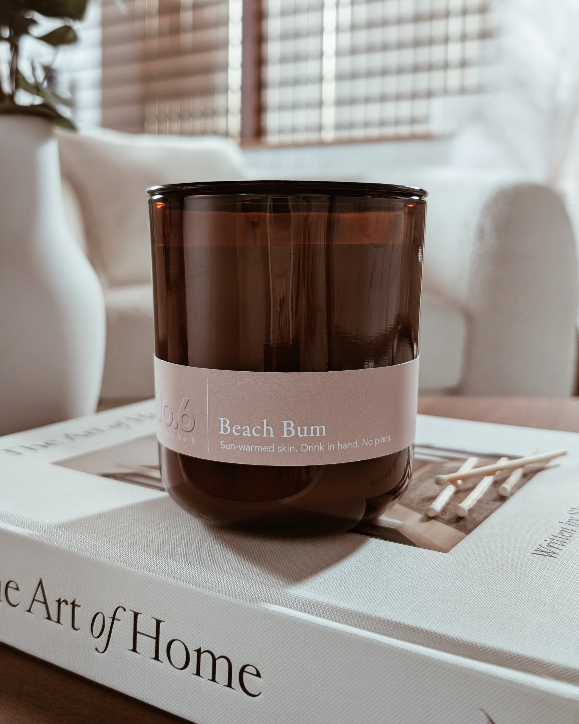 Amber glass candle labeled Beach Bum on a book in a cozy indoor setting.