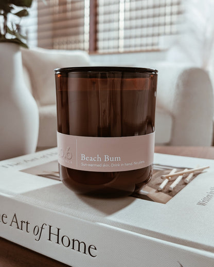 Amber glass candle labeled Beach Bum on a book in a cozy indoor setting.