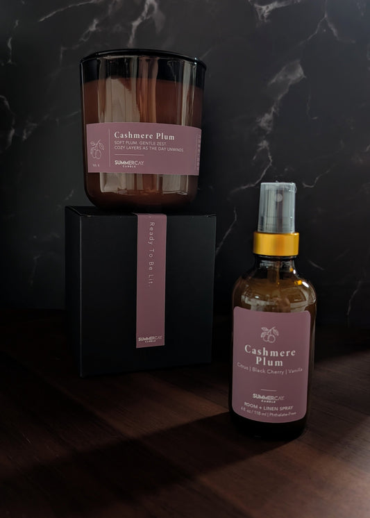 Candle and bottle labeled 'Cashmere Plum' on a dark surface