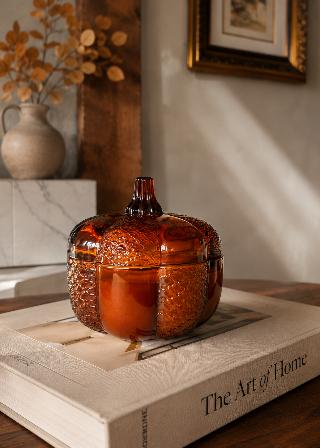 An amber glass pumpkin-shaped lidded container with a textured surface, displayed on a book in a warm, sunlit home interior.