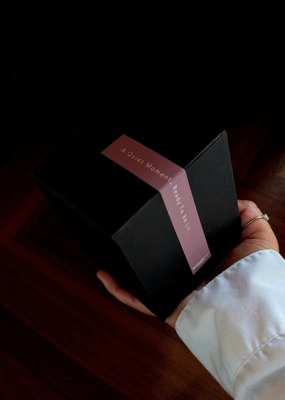 Hand holding out a black gift box with a label and a dark background.