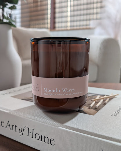Moonlit Waves scented candle in an amber vessel on top of a book in a cozy indoor setting. 