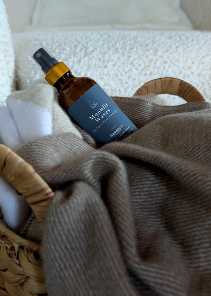Room spray bottle in a woven basket with soft blanket and a white background.