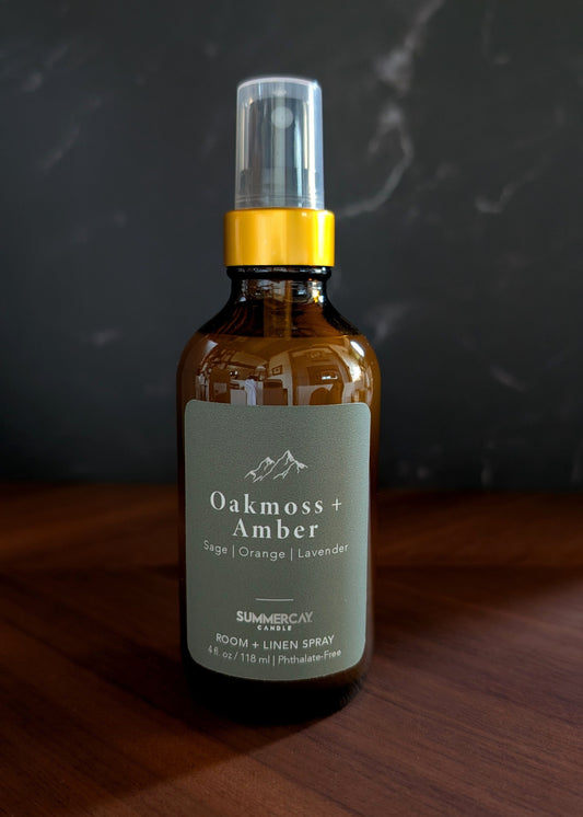 Oakmoss and amber room spray sitting on a wood table and dark background. 