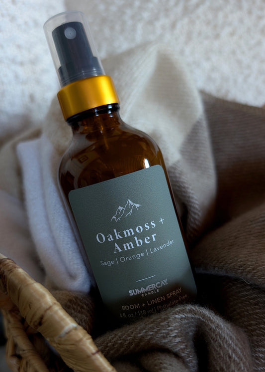 oakmoss + amber room spray sitting in a woven basket with a soft blanket.