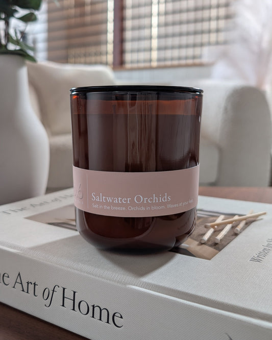 Saltwater Orchids scented candle in an amber vessel on top of a book in a cozy indoor setting. 
